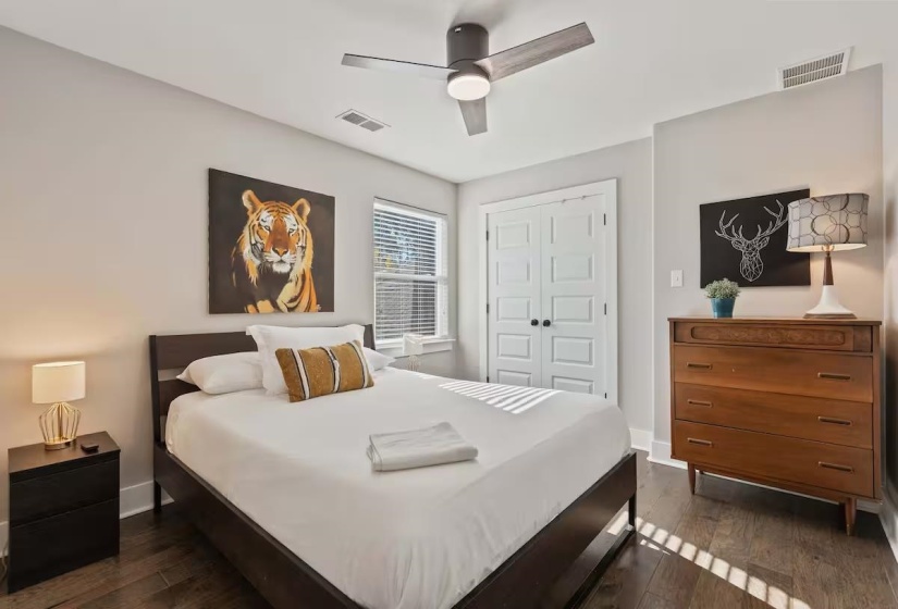 Bright interior space featuring wood-finish flooring, a ceiling fan with integrated lighting, a window with blinds, and white paneled bi-fold doors
