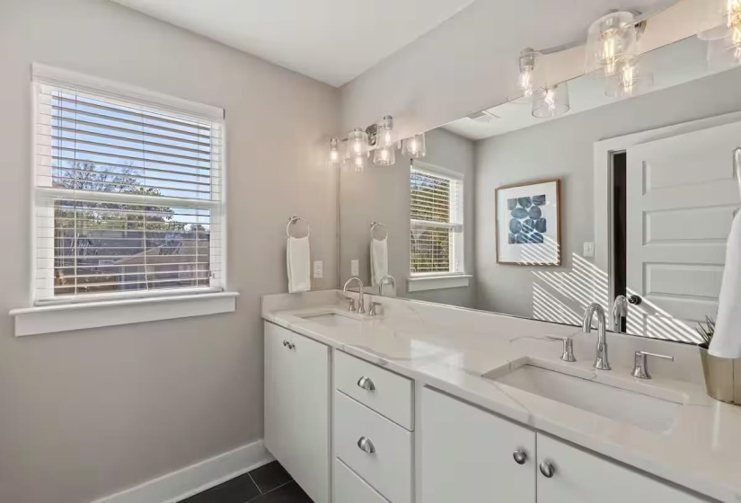 Dual vanity featuring white cabinetry and countertops with integrated sinks, chrome fixtures, and a large wall-mounted mirror