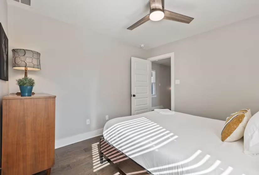 Bedroom featuring wood-finish flooring, a ceiling fan with integrated lighting, a solid wood paneled door, and neutral wall tones