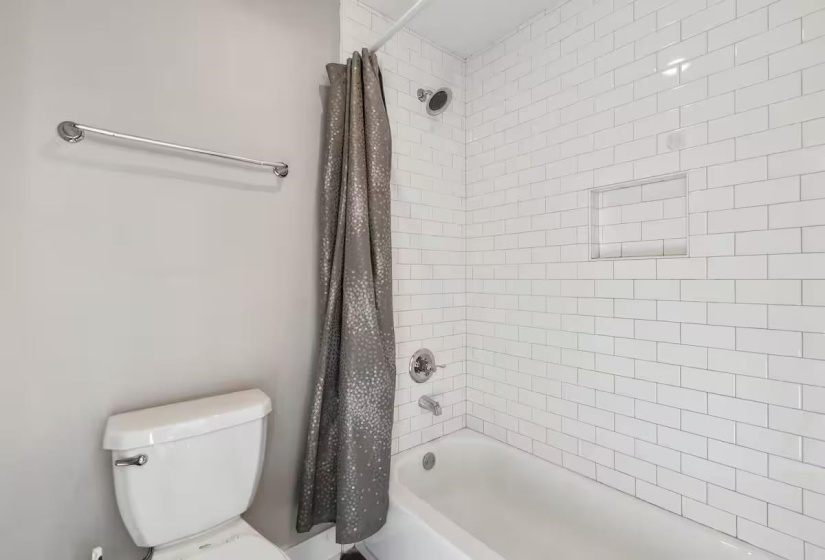 Bathtub with subway tile surround, recessed shower niche, and polished chrome fixtures