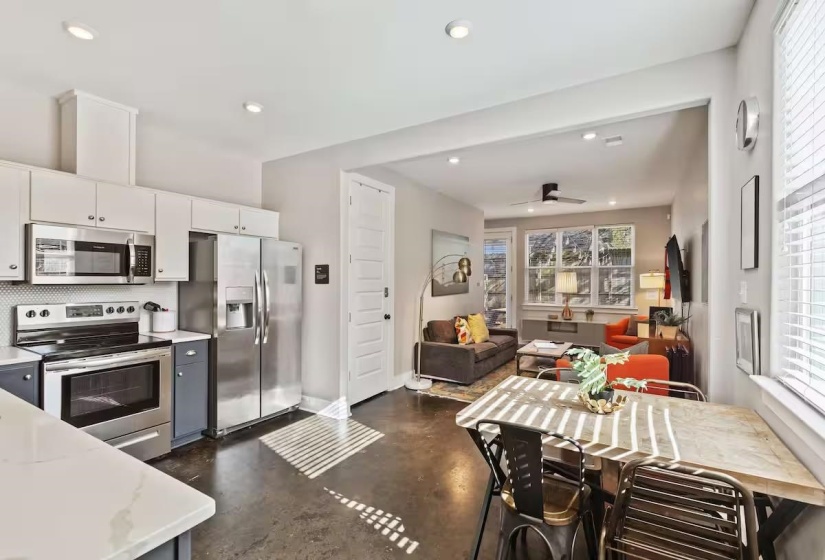 Open-concept living space featuring a modern kitchen with stainless steel appliances, white upper cabinetry, and dark lower cabinetry
