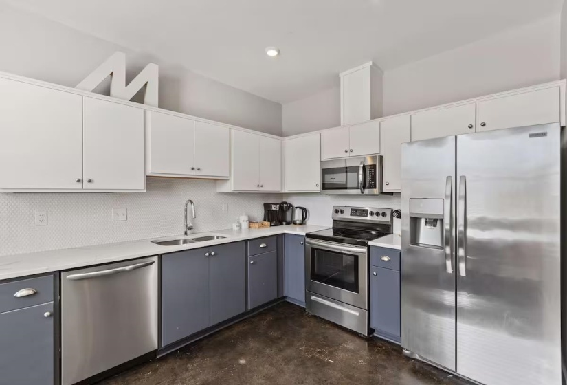 Modern kitchen featuring two-tone cabinetry, stainless steel appliances, white countertops, and a white penny tile backsplash