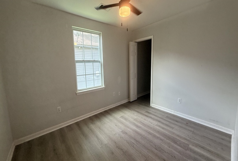 Spacious room featuring wood-finish flooring, light gray walls, a window with white trim, and a ceiling fan with integrated lighting