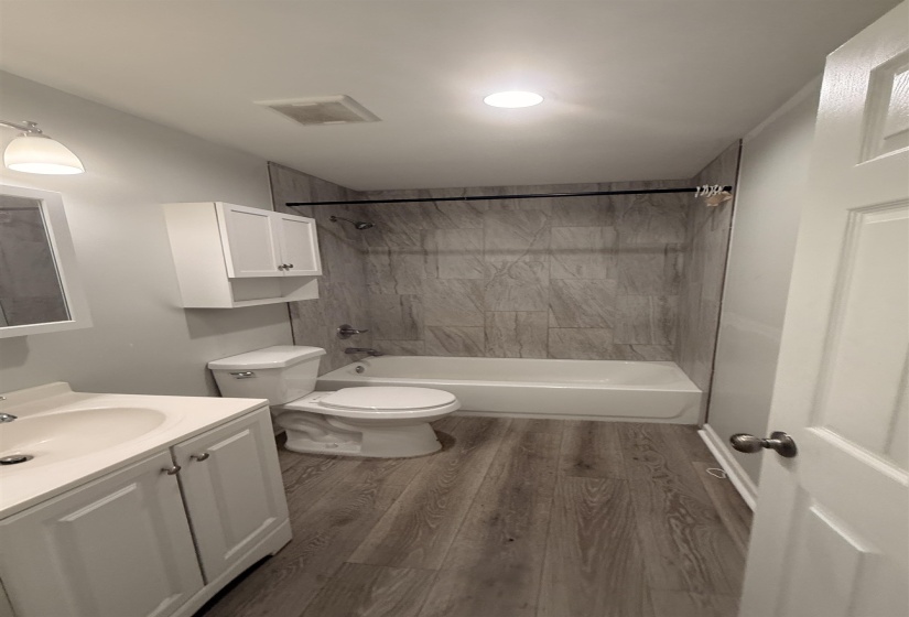 Full bathroom featuring a single vanity with under-sink storage, a white toilet, and a bathtub with a tiled surround