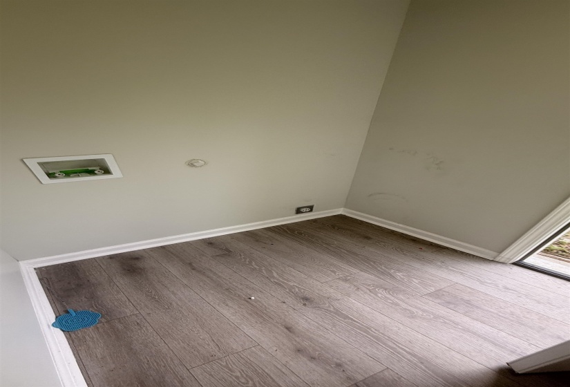 Utility area featuring wood-finish flooring, light grey walls, and a recessed water hookup box