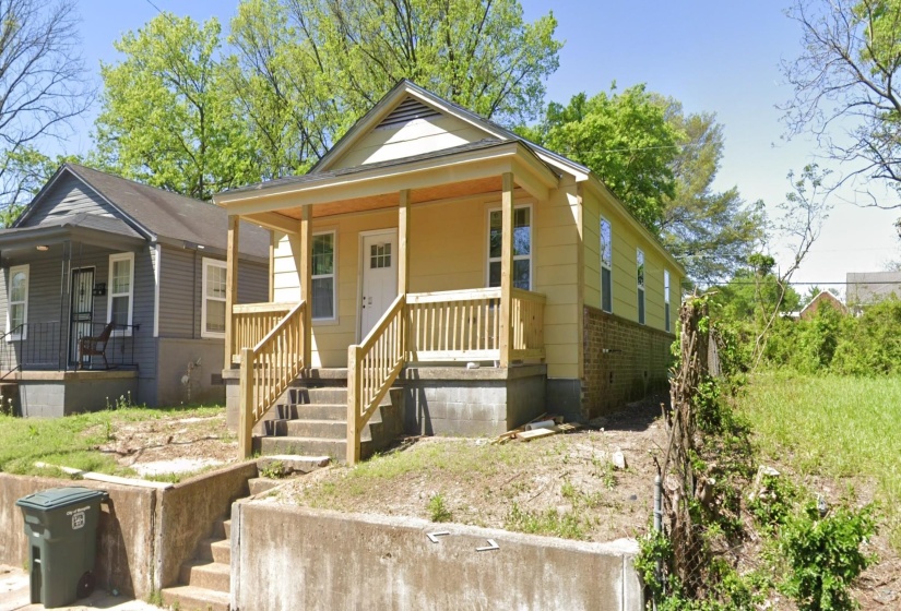 Yellow siding exterior featuring a covered porch with natural wood railings, concrete steps, and a white paneled front door