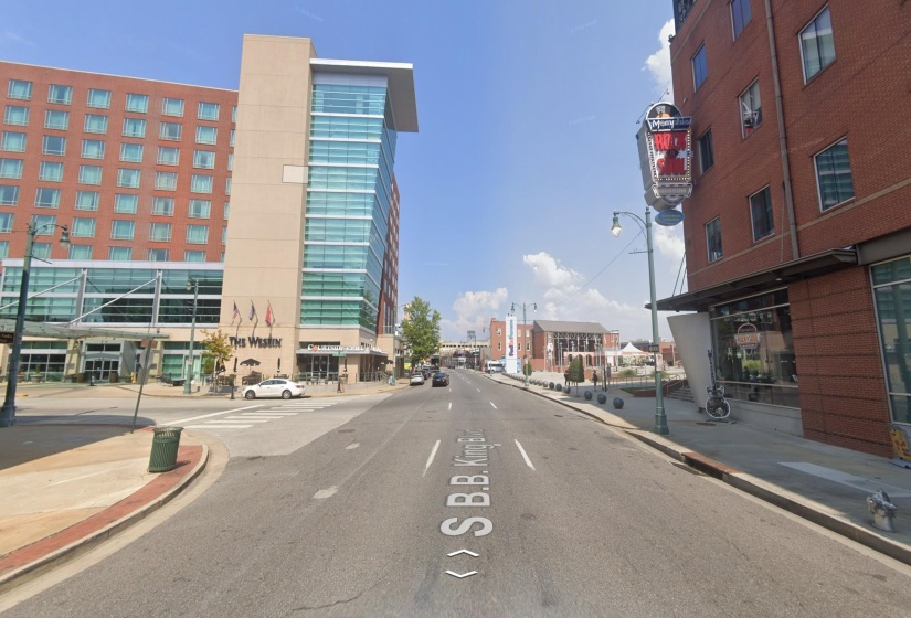 Street view featuring a multi-story building with a brick facade and extensive glazing, a prominent commercial sign, and pedestrian-friendly sidewalks