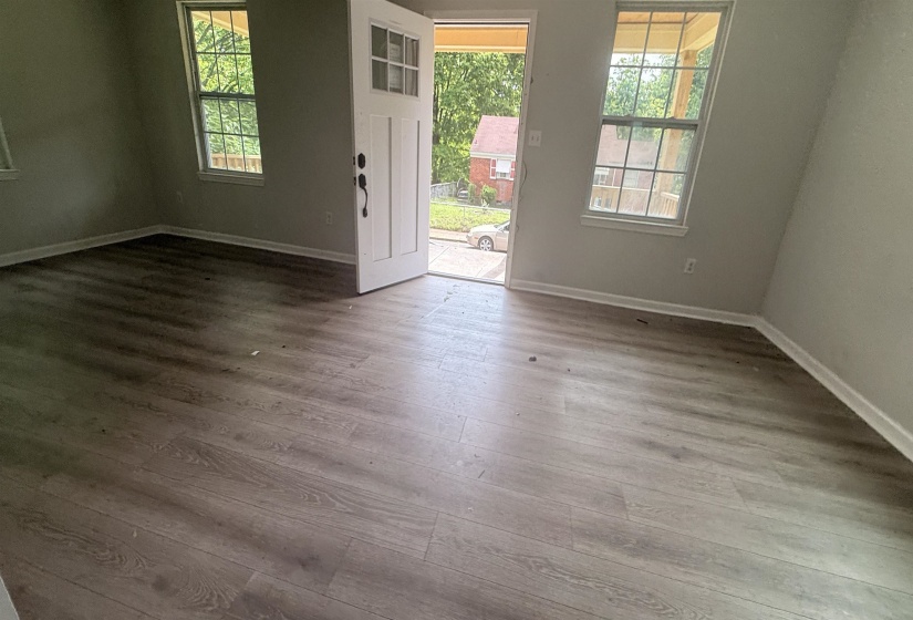 Spacious interior featuring wood-finish flooring, light grey walls, white baseboards, and multiple large windows with natural light