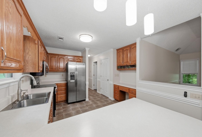 Kitchen featuring wood cabinetry, stainless steel appliances, a double basin sink with a pull-down faucet, vinyl flooring, and recessed and pendant lighting