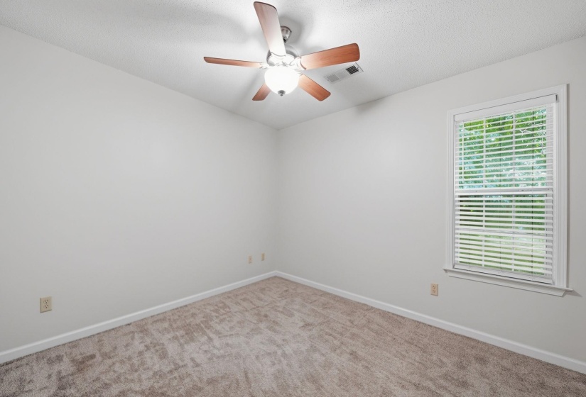 Bedroom featuring a textured carpet, white walls, and a ceiling fan with wood-finish blades