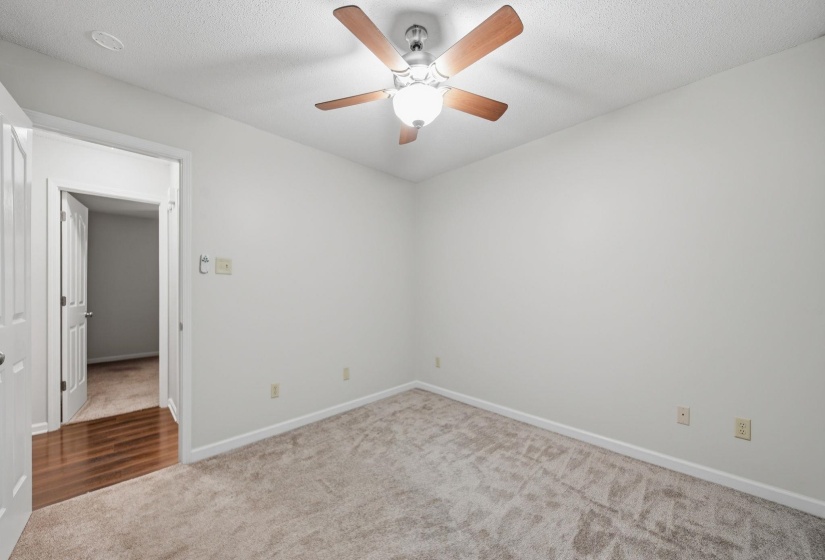 Bedroom featuring a textured carpet, white walls, and a ceiling fan with wood-finish blades