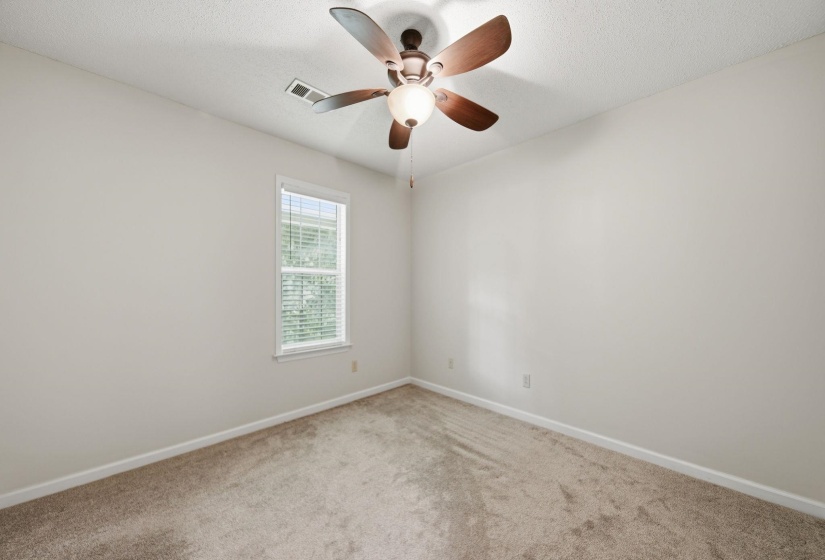 Bedroom featuring a textured carpet, white walls, and a ceiling fan with wood-finish blades