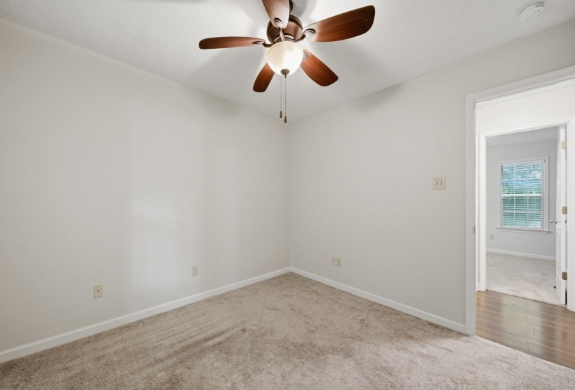 Bedroom featuring a textured carpet, white walls, and a ceiling fan with wood-finish blades