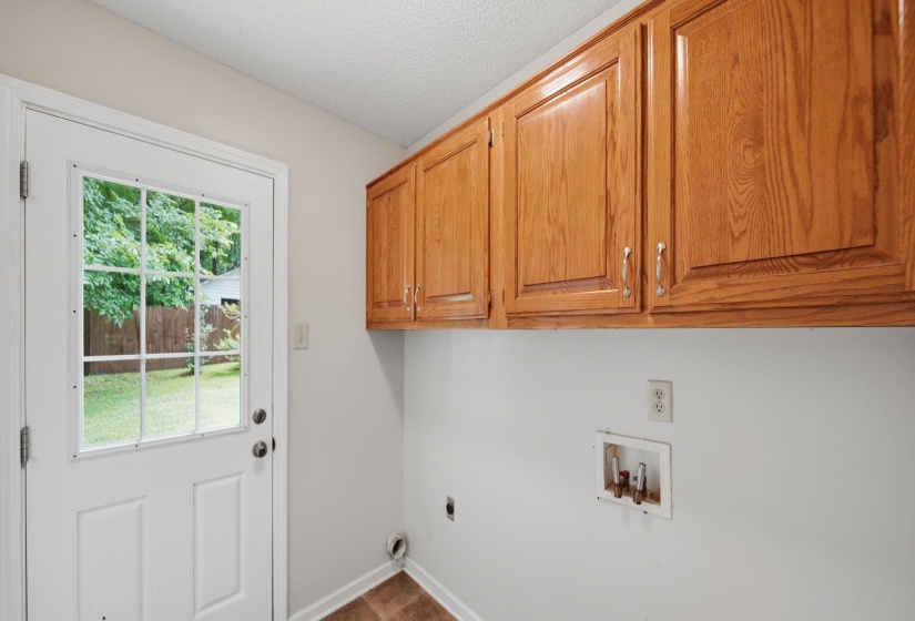Utility area featuring wood-finish cabinetry with silver-tone hardware, a paneled door with a grid-pattern glass insert, and vinyl flooring