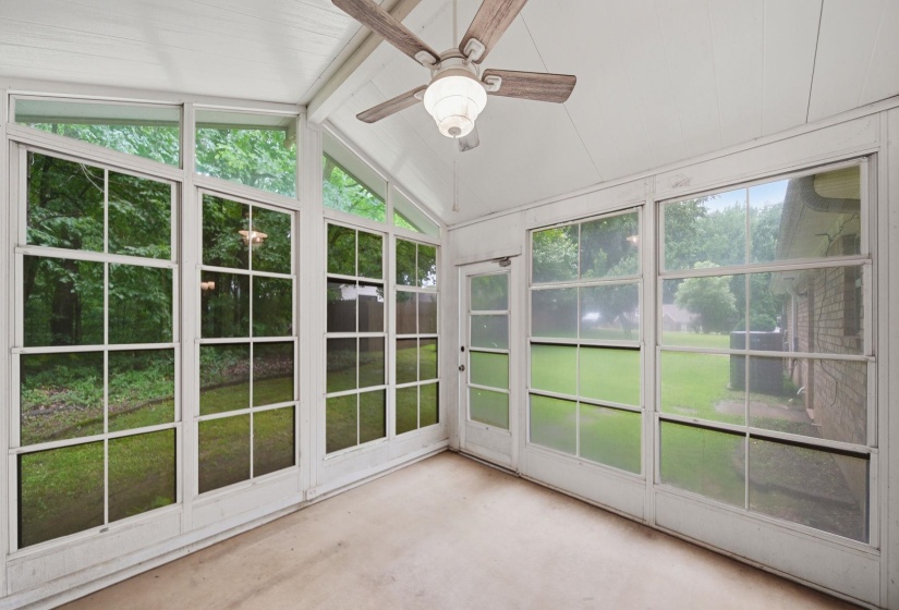 Enclosed sunroom featuring a pitched ceiling, wood-finish ceiling fan, full-height windows, and a dedicated exterior door