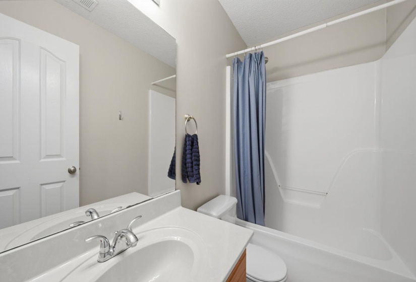 Bathroom featuring a white integrated sink, chrome faucet, wood-finish vanity, and a white shower-over-tub combination with a single-piece surround