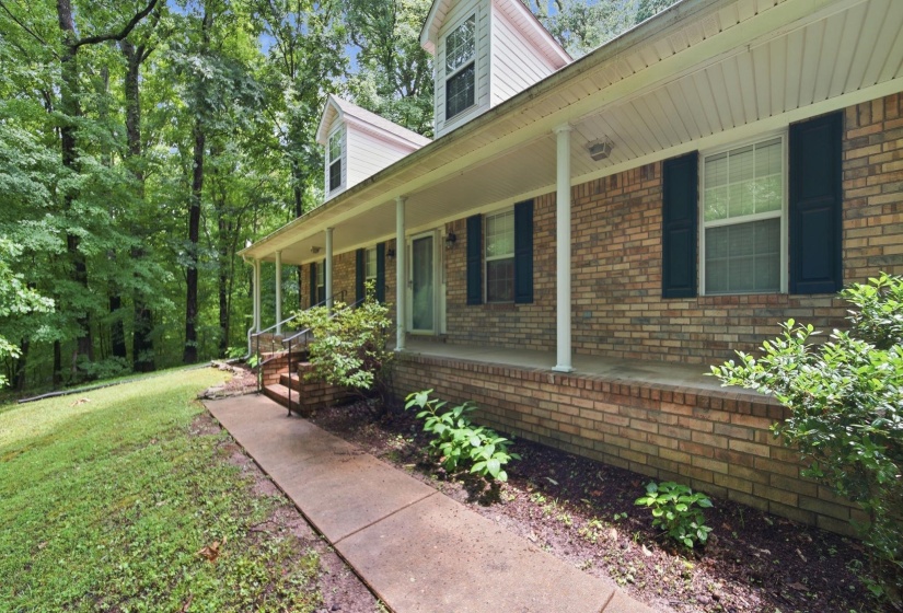Brick facade residence featuring a full-length covered porch, dark window shutters, and white vertical siding on dormer windows