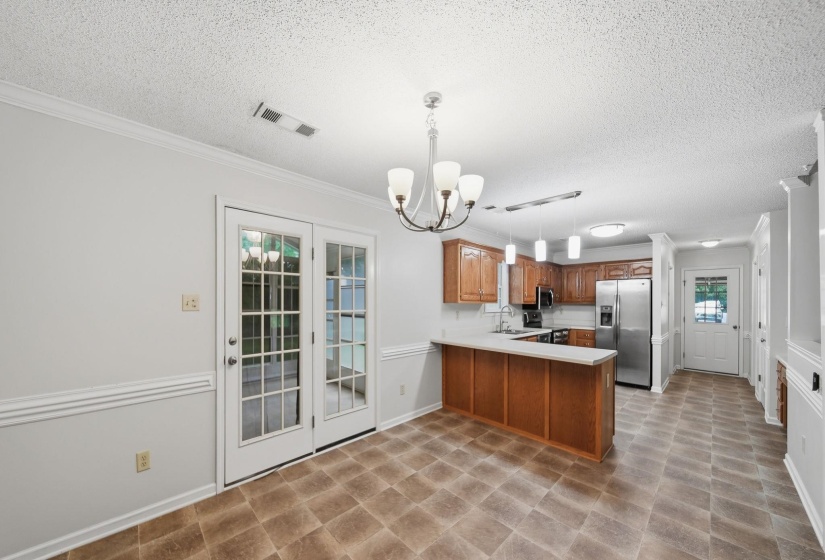 Open-concept kitchen and dining area featuring wood-finish cabinetry, stainless steel appliances, a breakfast bar, and double paneled glass doors