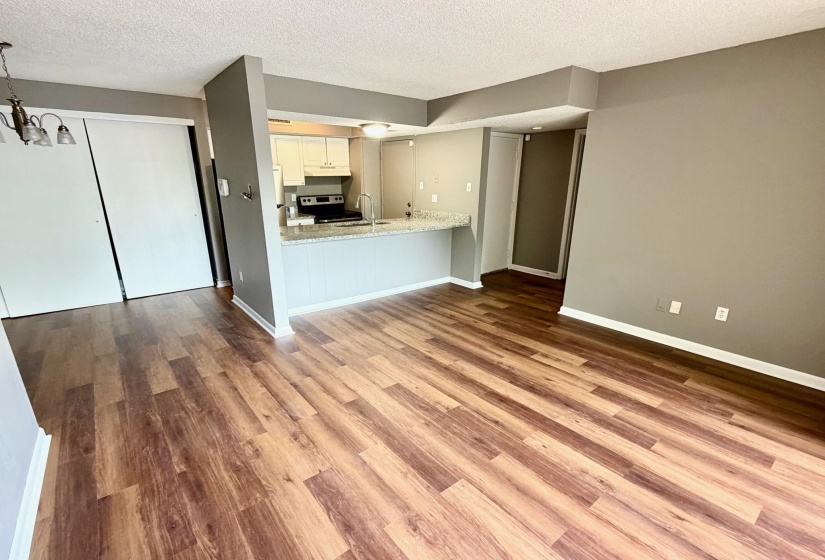 Open-concept living area featuring wood-finish flooring, a breakfast bar with stone-finish countertop, white cabinetry, and stainless steel appliances