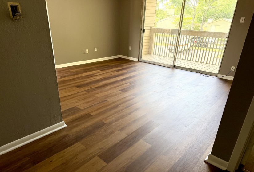 Spacious room featuring wood-finish flooring, neutral-toned walls, white baseboards, and a sliding glass door