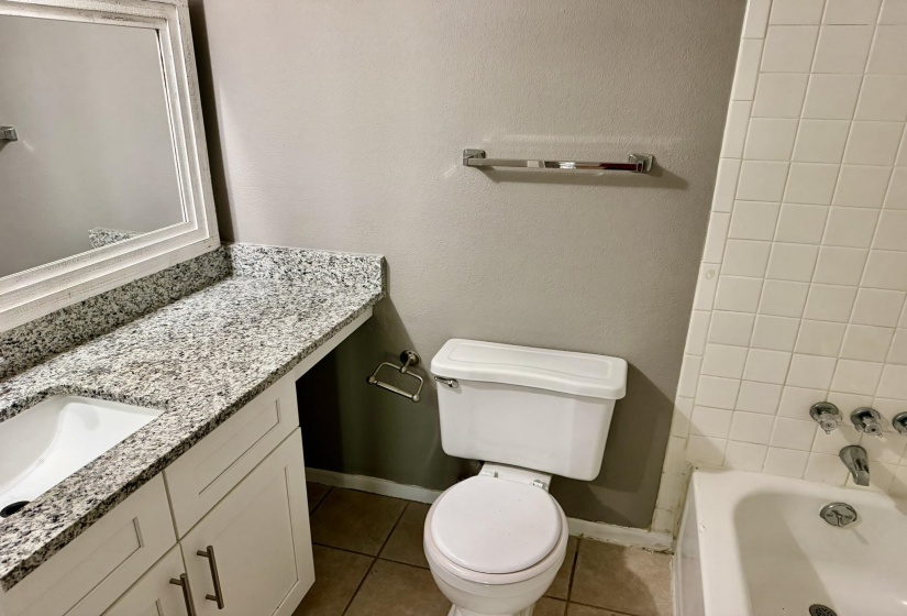 Bathroom featuring a white vanity with a speckled countertop, a built-in sink, a framed mirror, and a white toilet