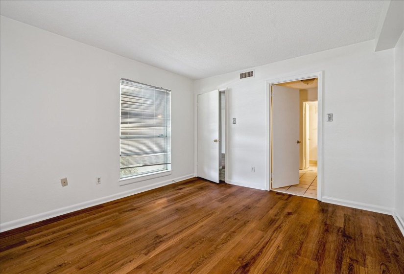 Room featuring wood-finish flooring, white walls, and a window with blinds