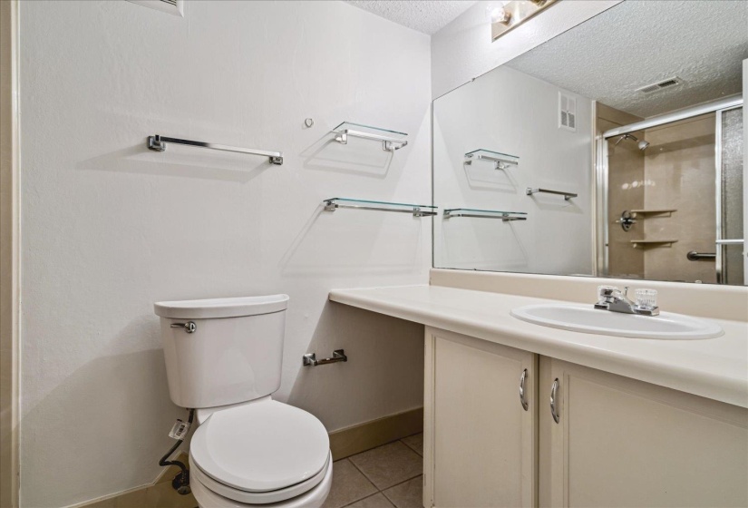 Bathroom featuring a white toilet, a vanity with an integrated sink, a large wall-mounted mirror, and a shower enclosure with glass doors