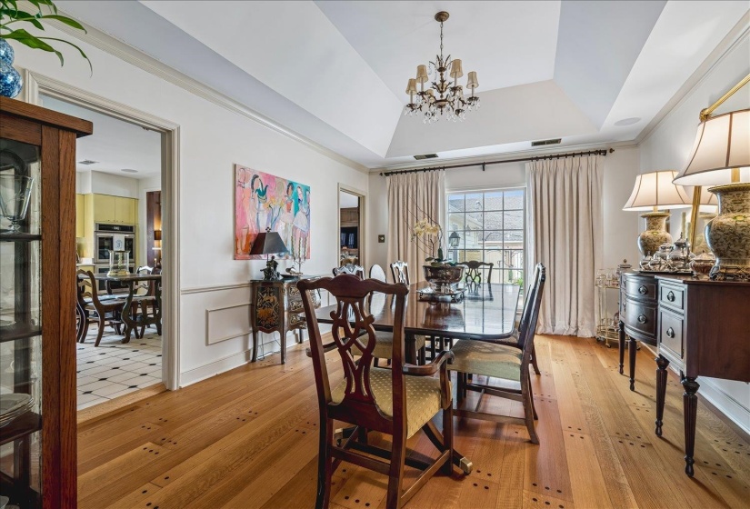 Dining area featuring wood-finish flooring, a tray ceiling with a chandelier, and a large window with drapes