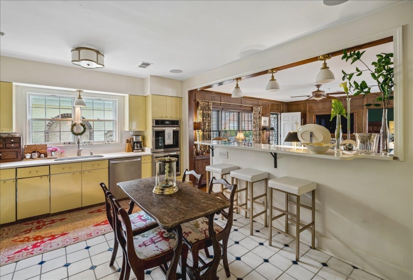 Bright kitchen featuring yellow cabinetry, white countertops, built-in double ovens, and a pass-through bar with pendant lighting