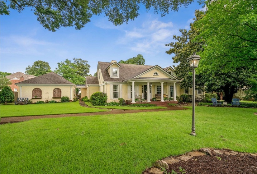 Traditional-style residence featuring a dormer window, covered front porch with white columns, and an expansive lawn