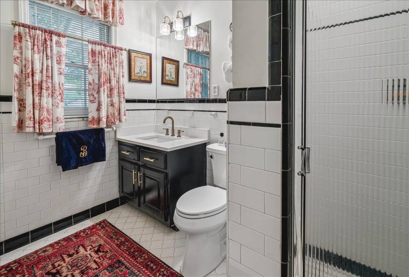 Bathroom featuring white subway tile walls with black trim, a dark wood-finish vanity with a white countertop and basin sink, a wall-mounted mirror, and a fluted glass shower enclosure