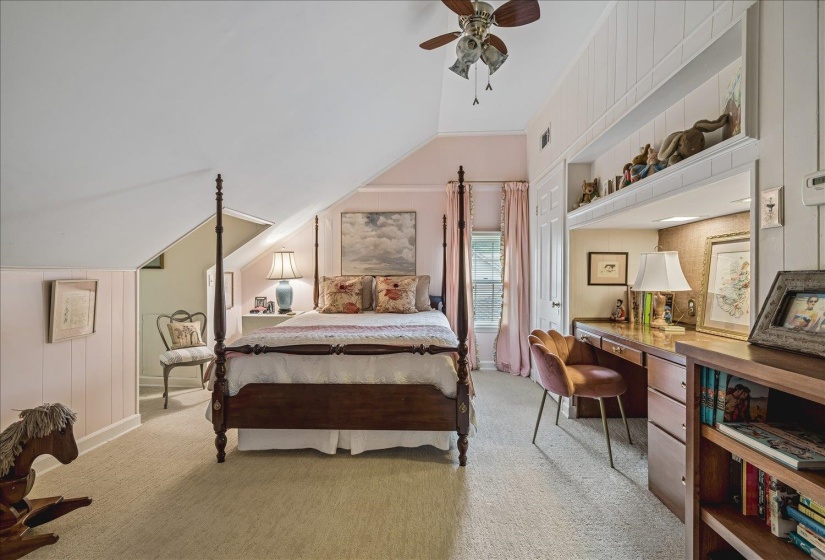 Carpeted room featuring sloped ceilings, a four-poster bed, and a built-in desk with shelving