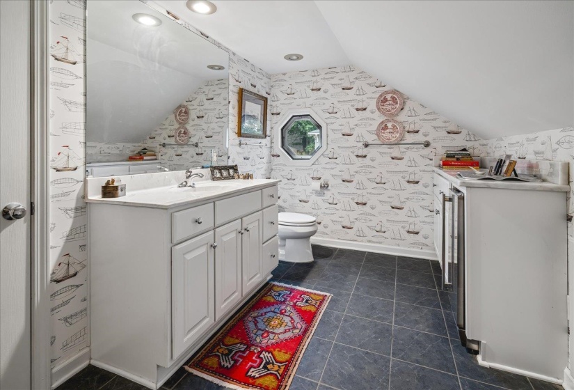 Bathroom featuring a white vanity with an integrated sink and white countertop, dark tiled flooring, and an octagonal window