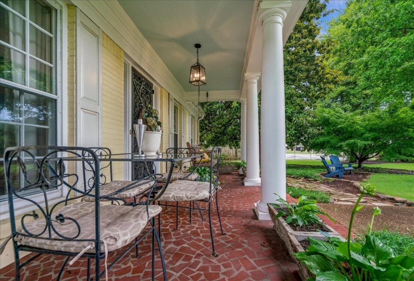 Expansive covered porch featuring a red brick-patterned floor, white colonial columns, a pale yellow brick facade, and a decorative hanging lantern fixture