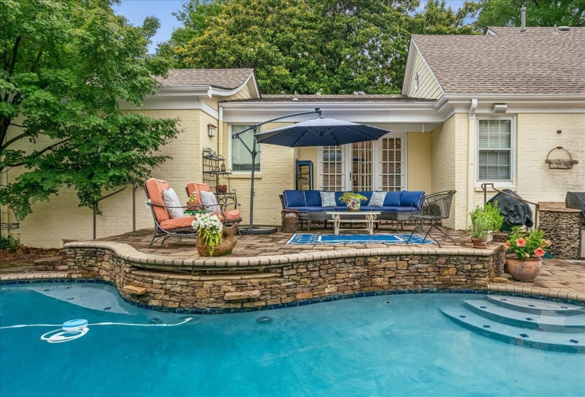 Outdoor living space featuring a swimming pool with integrated steps, a stone-accented pool wall, and a paver patio