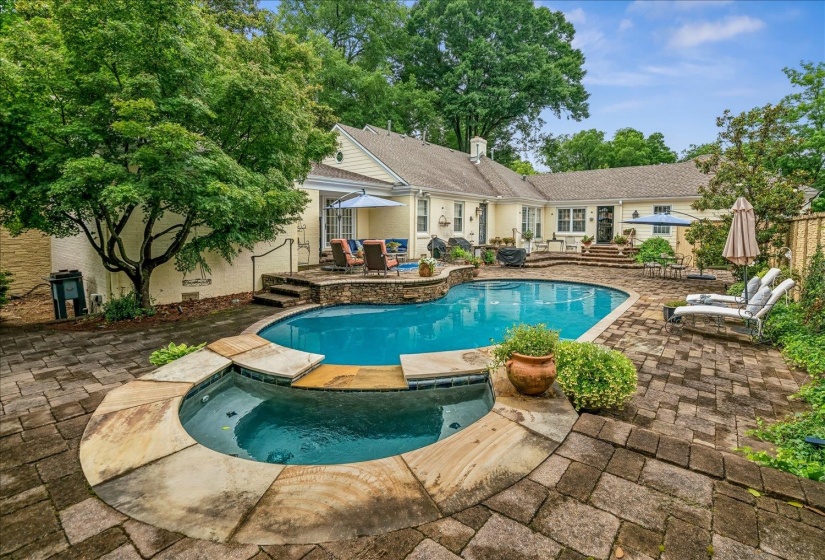 Expansive paver patio surrounding a custom-shaped swimming pool with an integrated spa