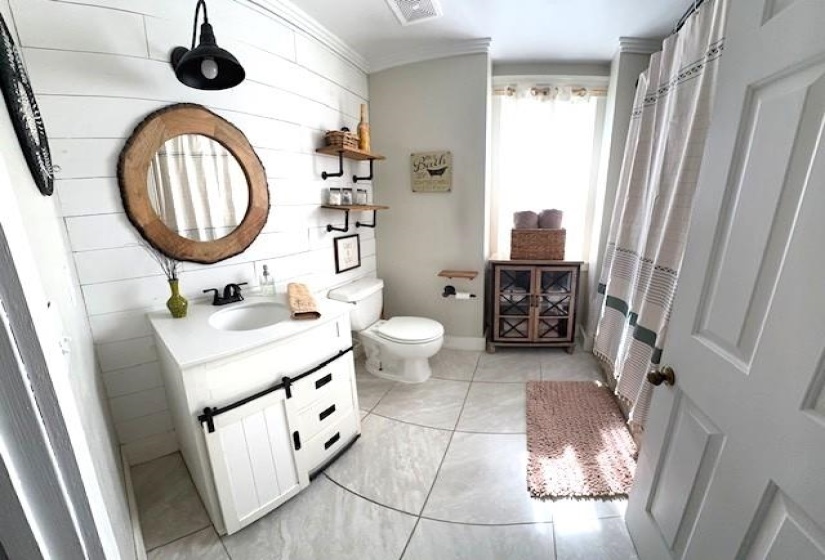 Bathroom featuring a white vanity with sliding barn door accent, contemporary black faucet, and a round wood-finish mirror