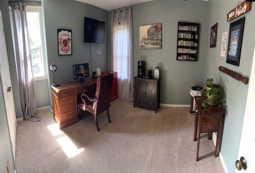 Carpeted room featuring a built-in wall-mounted television, two windows with drapery, and a functional built-in wall rack
