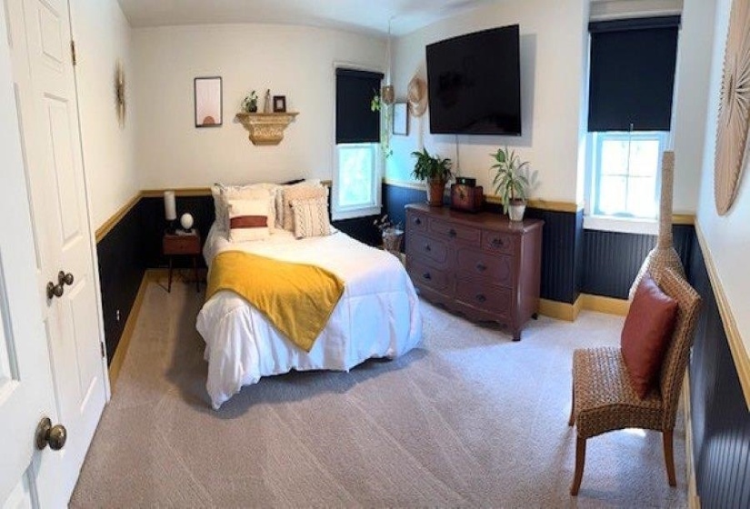 Carpeted room featuring wainscoting with a dark finish and light trim, two windows with dark roller shades, and a ceiling-mounted light fixture