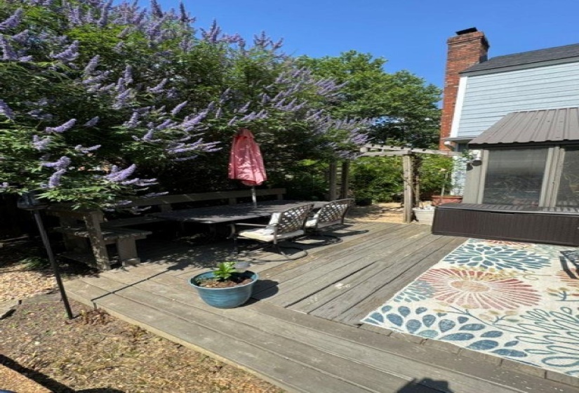 Wood-finish deck featuring a built-in bench seating area, a pergola, and mature flowering shrubs