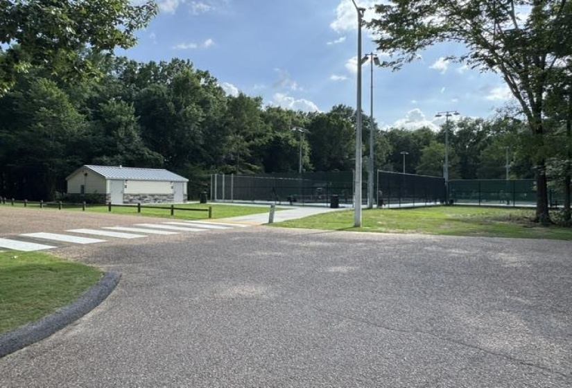 Outdoor tennis courts with chain-link fencing, surrounded by mature trees