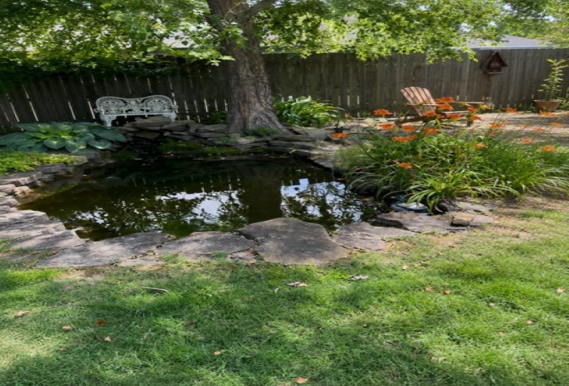 Backyard featuring a tranquil pond, stone landscaping, mature shade tree, and established perennial plantings