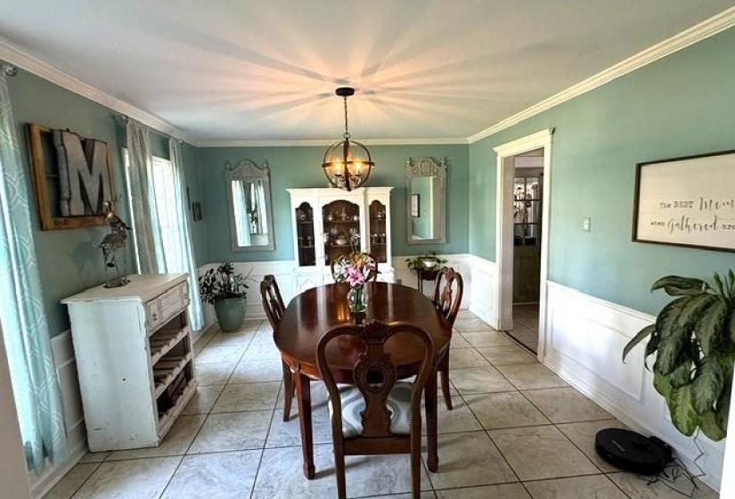 Spacious dining area featuring neutral tile flooring, wainscoting, crown molding, and an overhead spherical chandelier