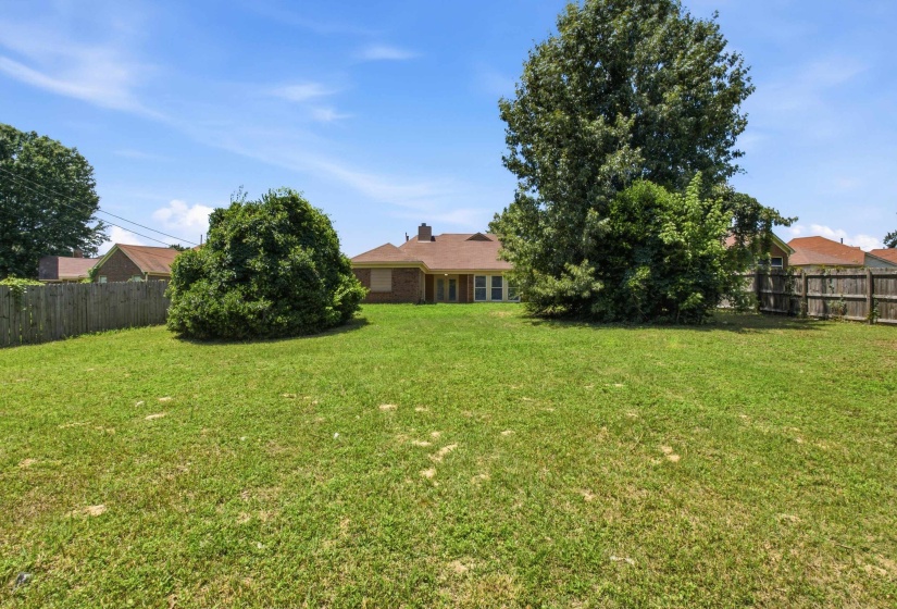 Expansive rear yard featuring a wooden privacy fence, mature trees, and a brick exterior residence with a shingled roof