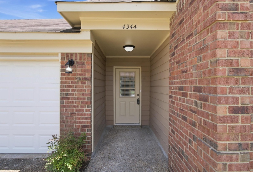 Welcoming entryway featuring a neutral-toned door with frosted glass, overhead lighting, and a covered porch