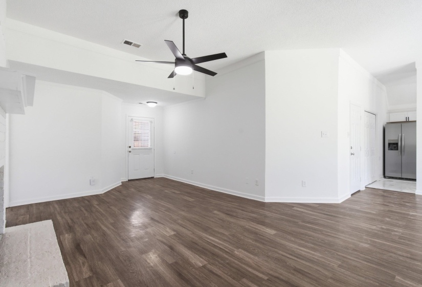 Spacious room featuring wood-finish flooring, a contemporary black ceiling fan, and a painted brick fireplace