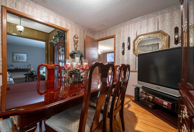 Hardwood flooring and decorative wallpaper characterize this interior space, featuring a wood-trimmed doorway