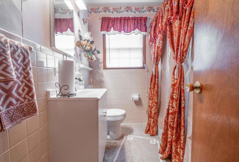 Bathroom featuring a white vanity with integrated sink, a wall-mounted mirror, white square wall tiling, and a window with blinds