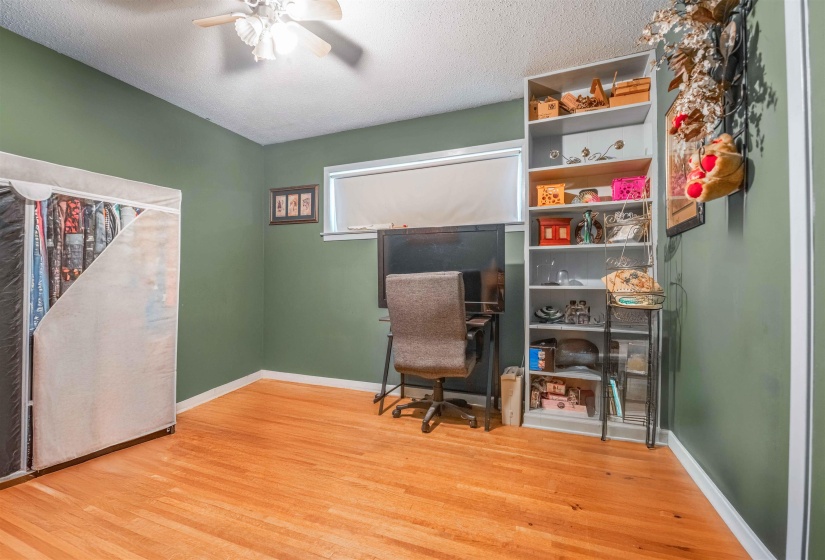 Room featuring wood-finish flooring, a ceiling fan, and a built-in shelving unit
