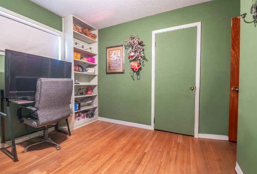 Interior space featuring wood-finish flooring, a built-in shelving unit, and a window with a roller shade